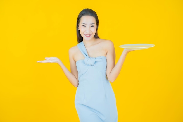 Portrait beautiful young asian woman smile with empty plate dish on yellow