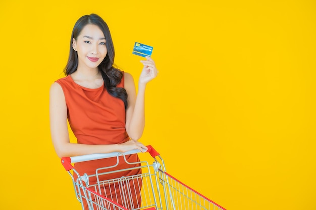 Ritratto bella giovane donna asiatica sorriso con cesto della spesa dal supermercato su yellow