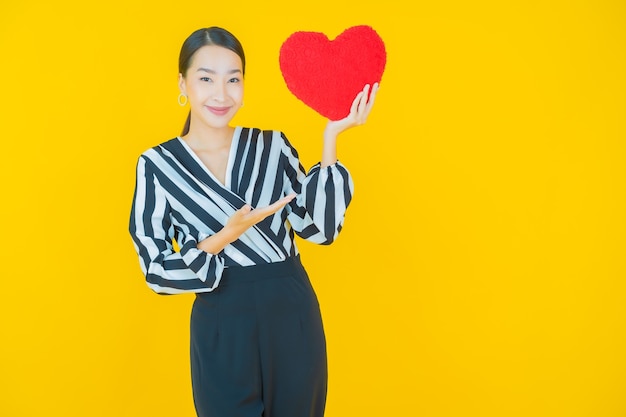 Portrait beautiful young asian woman smile with heart pillow shape on yellow