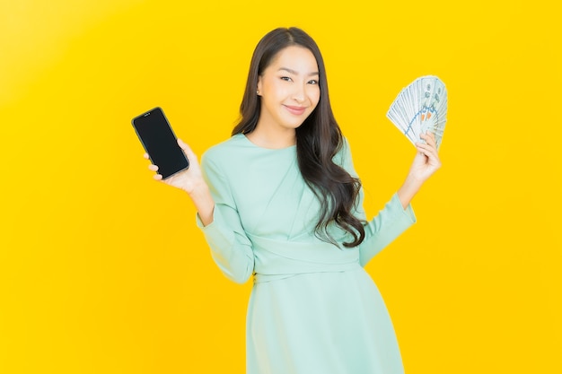Улыбка женщины портрета красивая молодая азиатская с большим количеством наличных денег и денег на желтом