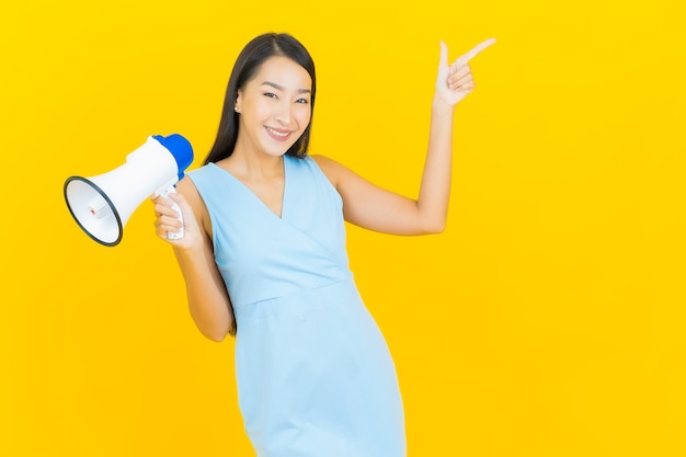 Portrait beautiful young asian woman smile with megaphone on yellow color wall