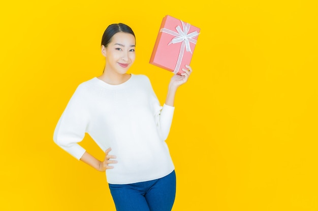 Portrait beautiful young asian woman smile with red gift box on yellow