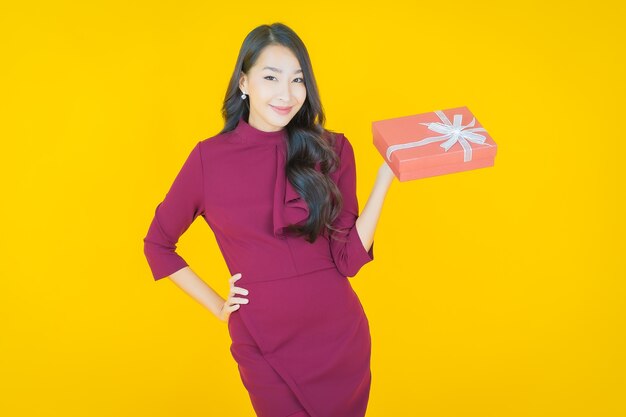 Portrait beautiful young asian woman smile with red gift box on yellow