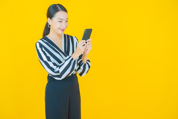 黄色のスマート携帯電話で笑顔美しい若いアジアの女性の肖像画