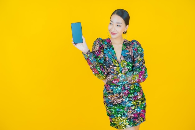 黄色のスマート携帯電話で笑顔美しい若いアジアの女性の肖像画