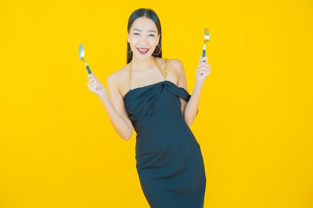 Портрет красивой молодой азиатской улыбки женщины с ложкой и вилкой