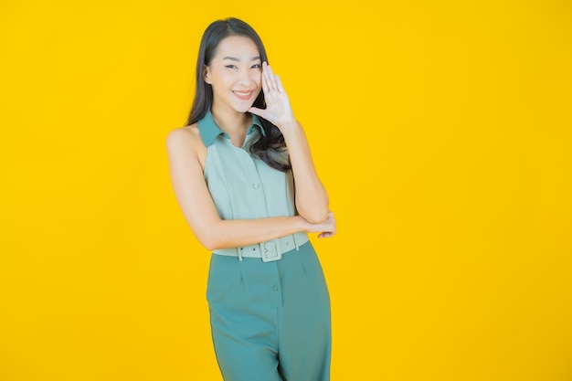 Portrait of beautiful young asian woman smiles doing action on yellow wall