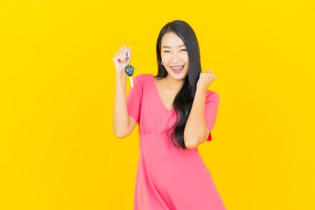 Portrait beautiful young asian woman smiles with car key on yellow wall