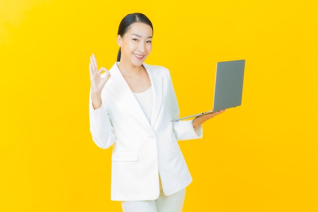 Portrait beautiful young asian woman smiles with computer laptop on isolated wall