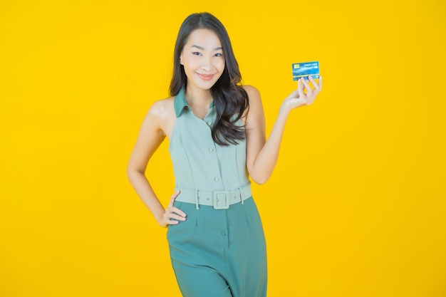 Portrait of beautiful young asian woman smiles with credit card on yellow wall