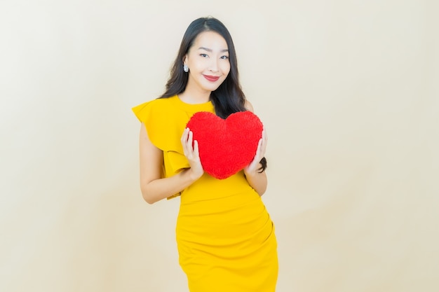 Portrait beautiful young asian woman smiles with heart pillow shape on beige wall