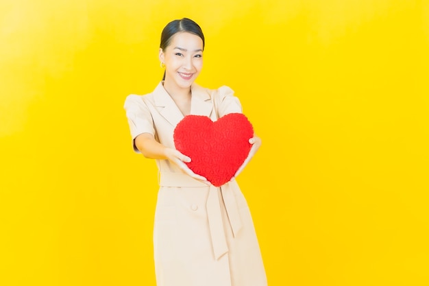 Portrait beautiful young asian woman smiles with heart pillow shape on color wall