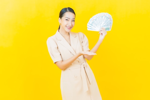 Portrait beautiful young asian woman smiles with a lot of cash and money on color wall