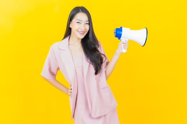 Portrait beautiful young asian woman smiles with megaphone on yellow yellow wall