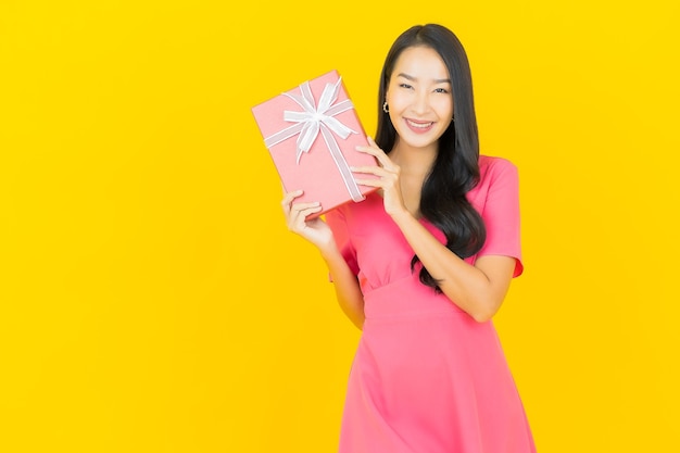 Portrait beautiful young asian woman smiles with red gift box on yellow wall