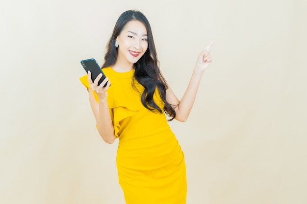 Portrait beautiful young asian woman smiles with smart mobile phone on beige wall