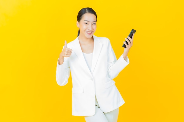 Portrait beautiful young asian woman smiles with smart mobile phone on color wall