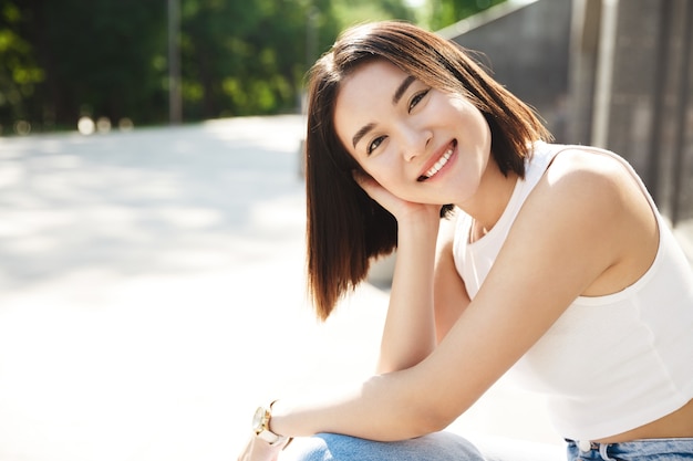 Portrait of beautiful young asian woman smiling while sitting outside on bench