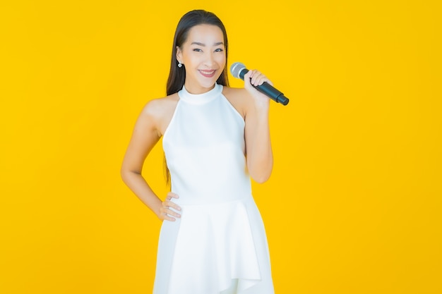 Портрет красивой молодой азиатской женщины использует микрофон для пения на желтом