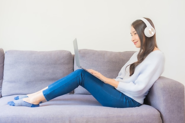 Portrait beautiful young asian woman using smart mobile phone and headphone for listen music in living room