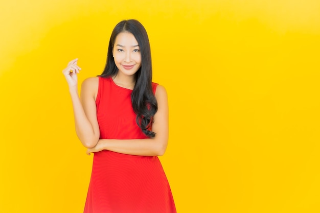 Portrait beautiful young asian woman wear red dress smile with action on yellow wall