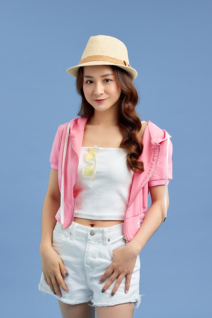 A portrait of a beautiful young Asian woman wearing a hat and sunglasses over blue background. Fashion, style, beauty, optics.