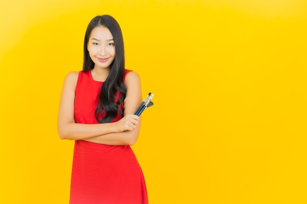 Portrait beautiful young asian woman with cosmetic brush on yellow wall