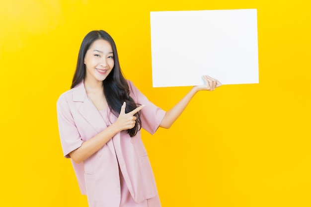 Portrait beautiful young asian woman with empty white billboard on yellow wall