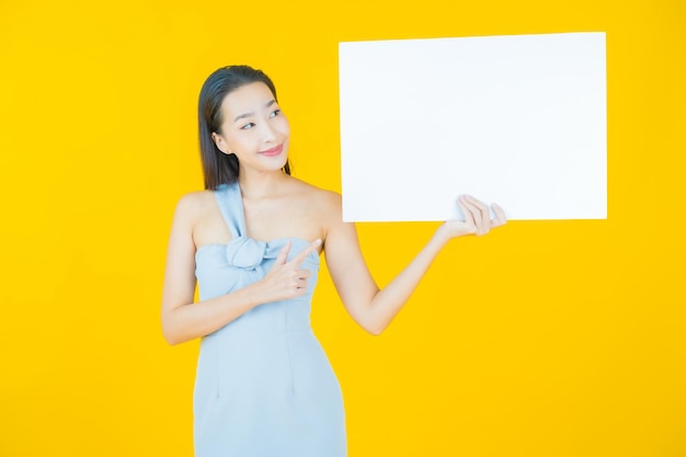 Portrait beautiful young asian woman with empty white billboard on yellow