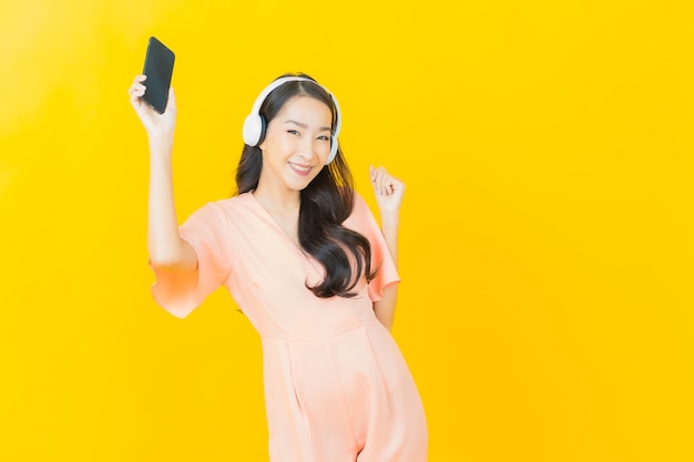 Portrait beautiful young asian woman with headphone and smart phone for listen music on yellow wall