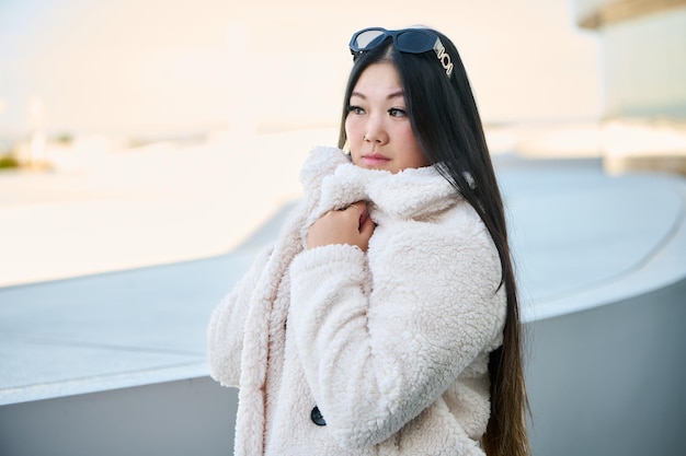 Foto ritratto di una bella giovane donna asiatica con lunghi capelli neri che indossa un cappotto e occhiali da sole