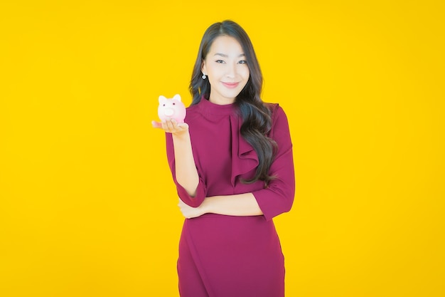 Portrait beautiful young asian woman with piggy bank on yellow