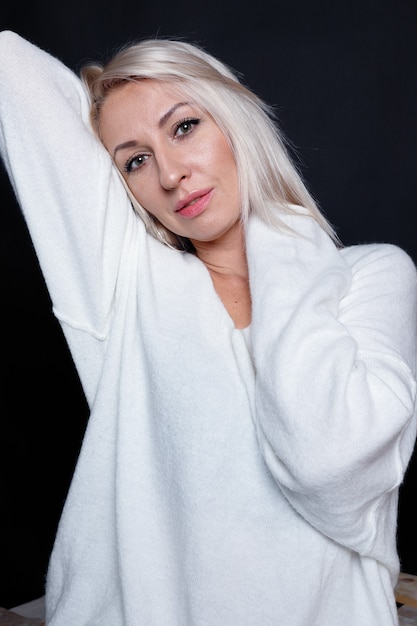 Портрет красивой молодой привлекательной женщины в белом свитере с голубыми глазами и длинными светлыми волосами.