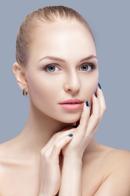 portrait of beautiful young blonde woman with blue eyes on grey background closeup.  Woman Touching her Face