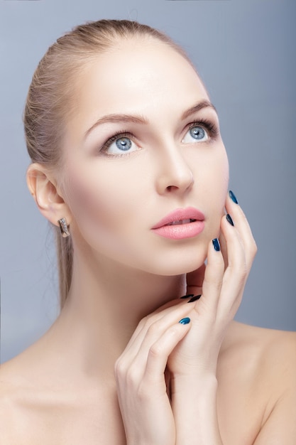 portrait of beautiful young blonde woman with blue eyes on grey background closeup.  Woman Touching her Face