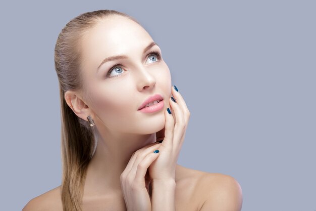 portrait of beautiful young blonde woman with blue eyes on grey background closeup.  Woman Touching her Face