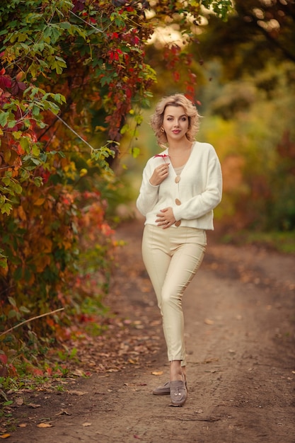 Portrait of a beautiful young blonde woman with a red leaf in her hands in an autumn park.