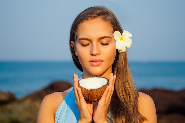 Portrait of beautiful young blue eyed woman with a coconut on the paradise shore of a tropical beach.perfect clean and healthy skin girl coco nut oil skin and hair moisturizing