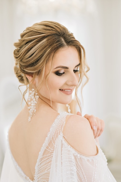 Ritratto di una bellissima giovane sposa in una stanza luminosa in un'atmosfera romantica. primo piano di trucco sposa e acconciatura