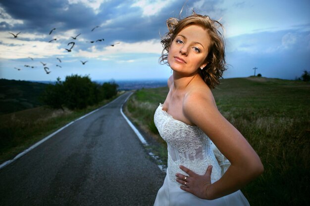 Foto ritratto di una bella giovane sposa in piedi sulla strada contro un cielo nuvoloso