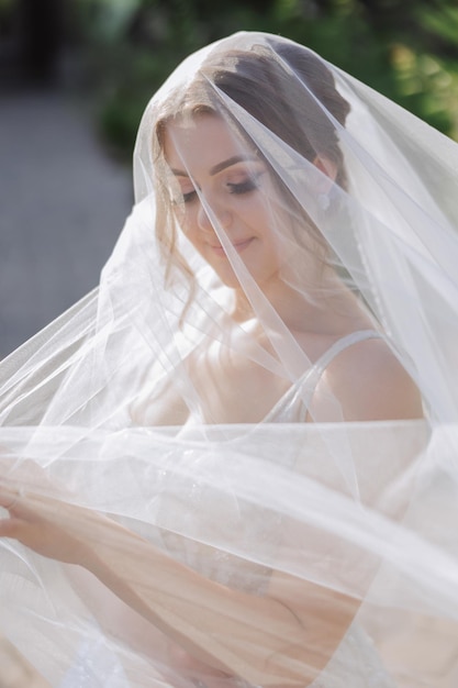 Foto ritratto di una bella giovane sposa in un vestito bianco con un lungo velo e una bellissima acconciatura sposa sorridente giorno di nozze sposa splendida matrimonio