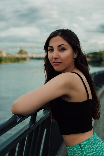 Photo portrait of a beautiful young brunette on the bridge by the river