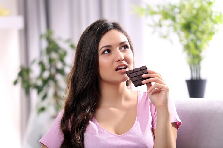 Photo portrait of beautiful young brunette with chocolate on sofa in the room , close up