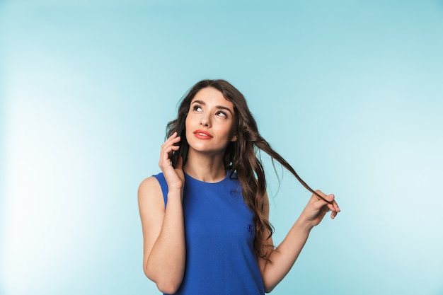 Portrait of a beautiful young brunette woman standing over blue, talking in mobile phone
