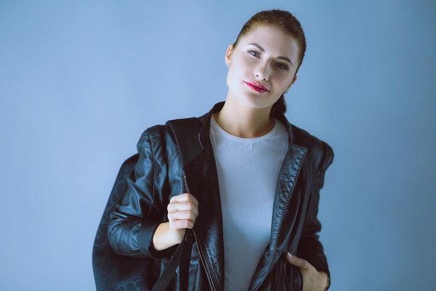 Portrait of beautiful young brunette woman in stylish black jacket on gray