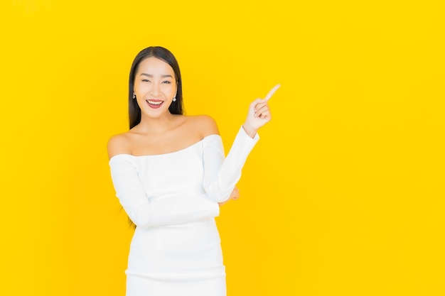 Portrait of beautiful young business asian woman smiling and pointing aside with white suit on yellow wall