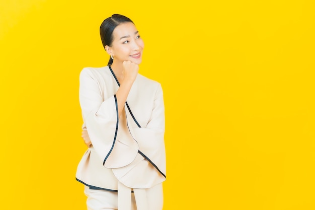 Photo portrait of beautiful young business asian woman smiling with white suit on yellow wall