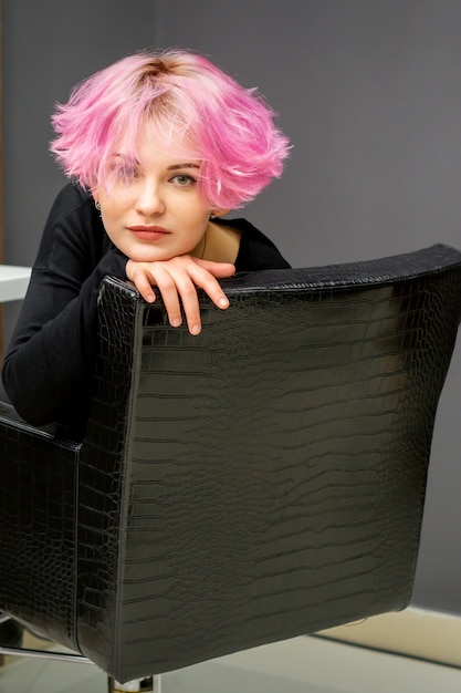 Portrait of a beautiful young caucasian woman with new short pink hairstyle sitting in a chair at a beauty salon