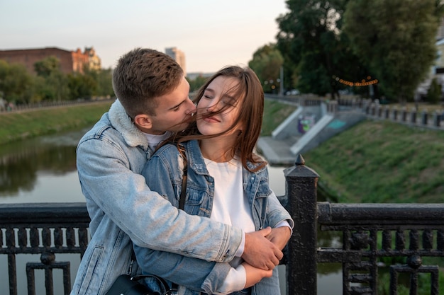 Portrait of beautiful young couple on the bridge. Guy gently embrace his beloved. Happy girl closed eyes. Romantic date in city.