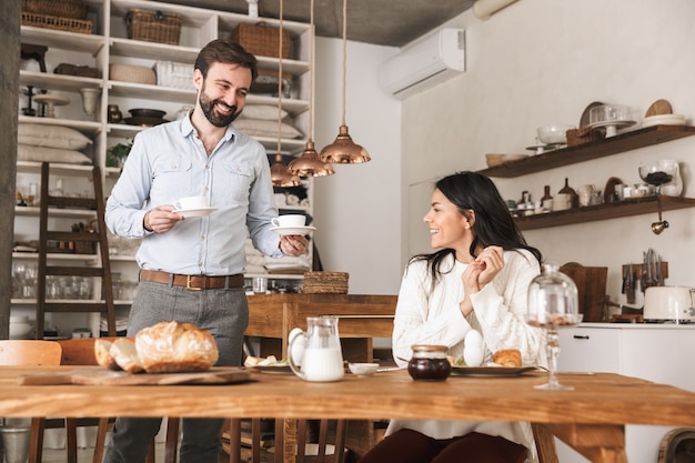 自宅のキッチンで朝食をしながらコーヒーを飲む美しい若いカップルの男性と女性の肖像画